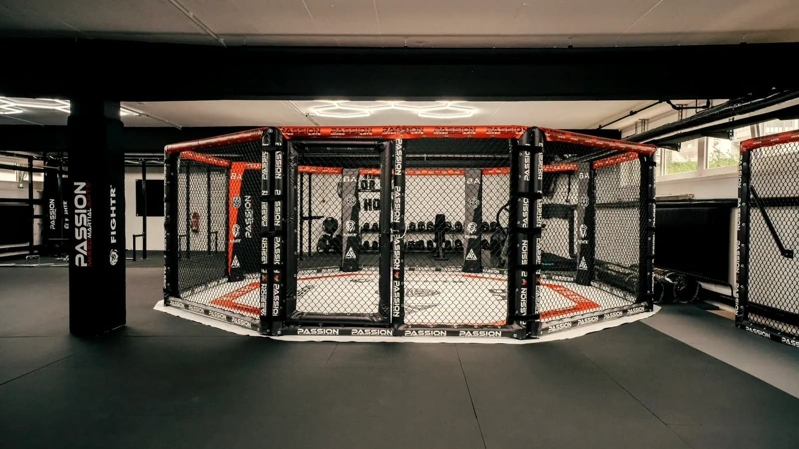 Octagon MMA cage with red padding in a large training hall